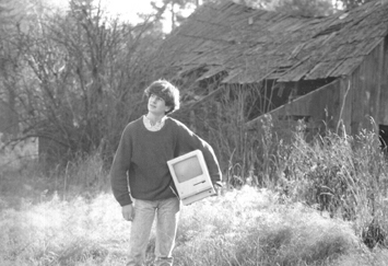 man in field holding old mac comptuer